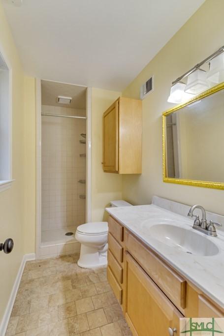 bathroom featuring vanity, a tile shower, and toilet