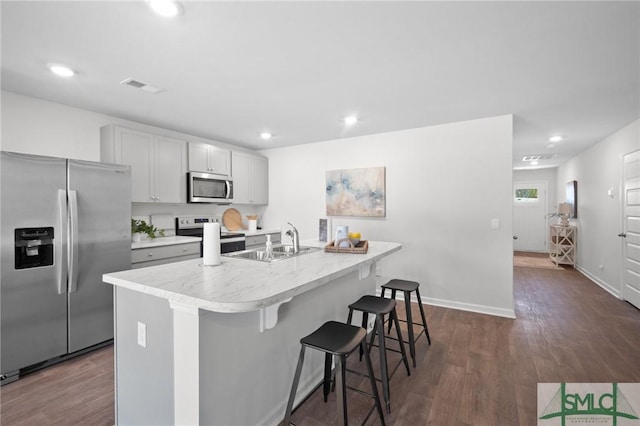 kitchen featuring an island with sink, sink, a kitchen bar, stainless steel appliances, and dark wood-type flooring