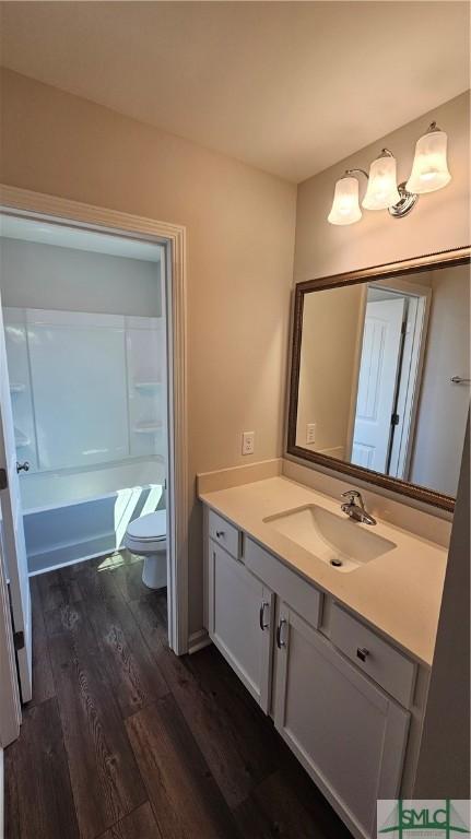 full bath with toilet, wood finished floors, vanity, and shower / bathtub combination