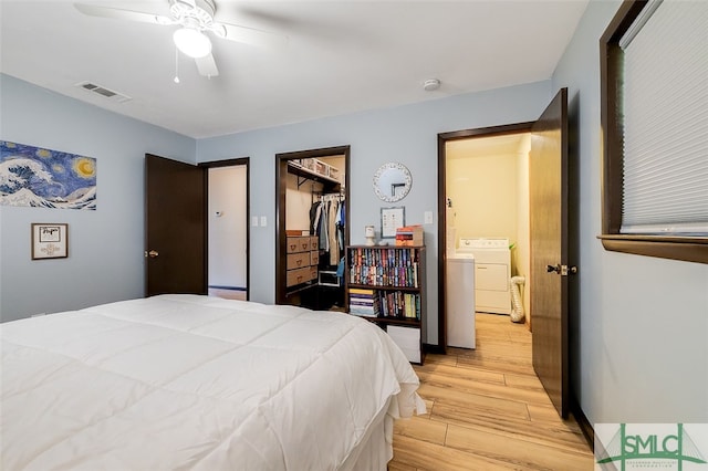 bedroom with light wood-type flooring, a spacious closet, ceiling fan, washing machine and dryer, and a closet