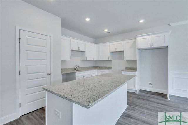 kitchen with white cabinetry, a center island, light stone countertops, dark wood-type flooring, and sink