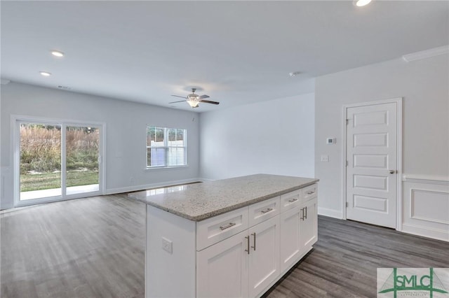 kitchen with light stone countertops, a kitchen island, ceiling fan, dark wood-type flooring, and white cabinetry