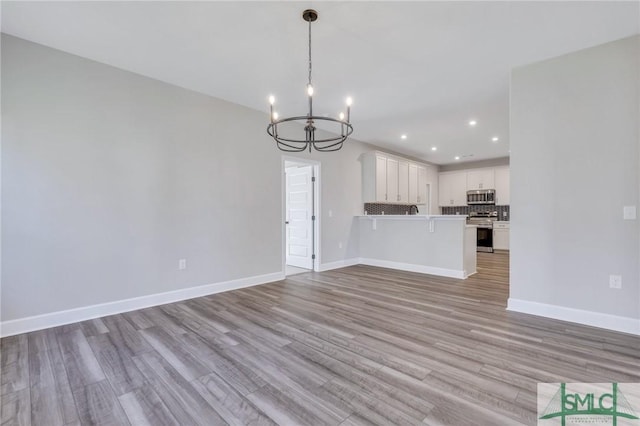 unfurnished living room with light wood-type flooring and an inviting chandelier