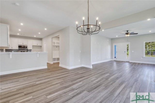 unfurnished living room with ceiling fan with notable chandelier and light hardwood / wood-style flooring