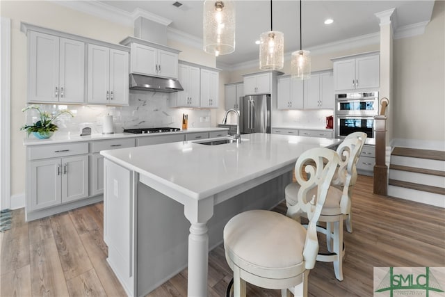 kitchen with sink, stainless steel appliances, backsplash, a center island with sink, and light wood-type flooring