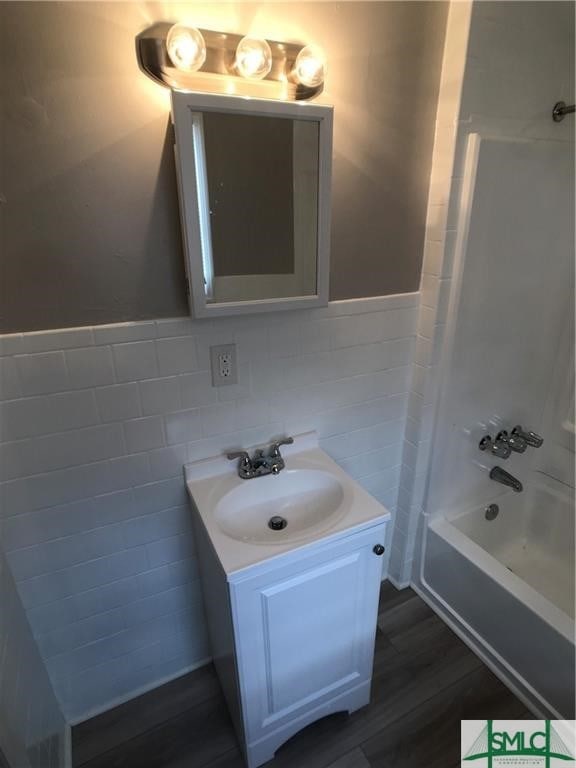 bathroom with tasteful backsplash, hardwood / wood-style floors, tub / shower combination, tile walls, and vanity