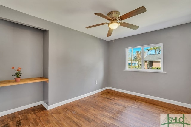 spare room featuring built in desk, wood-type flooring, and ceiling fan