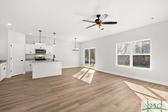 kitchen featuring ceiling fan with notable chandelier, appliances with stainless steel finishes, white cabinetry, hanging light fixtures, and a kitchen island with sink