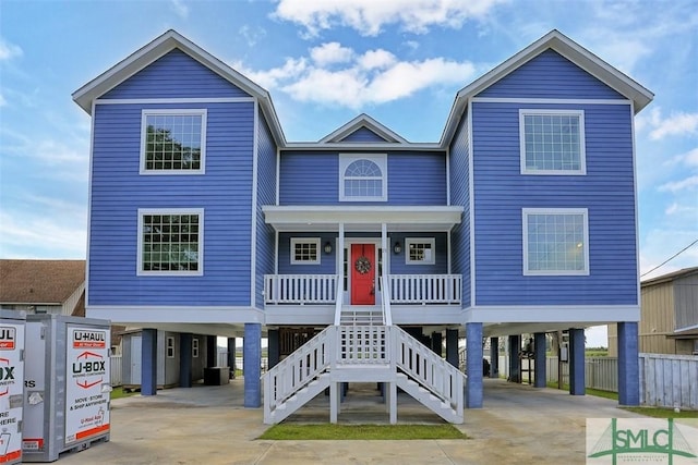 raised beach house with a carport, concrete driveway, a porch, and stairs