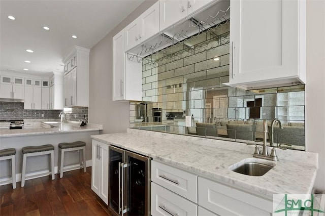 kitchen with beverage cooler, light stone counters, white cabinets, and dark wood-type flooring