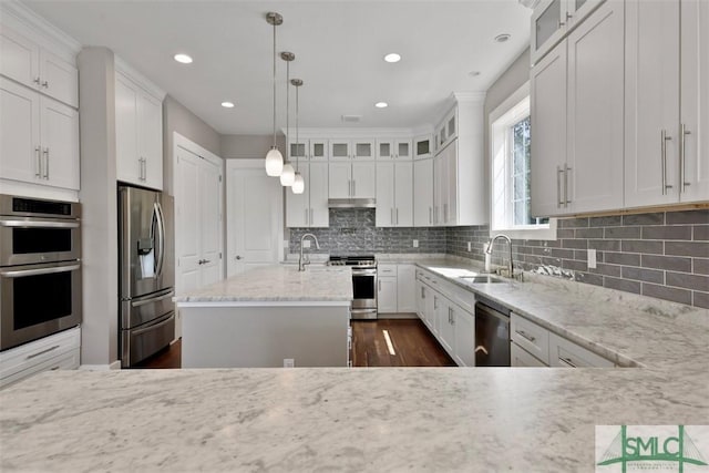 kitchen featuring appliances with stainless steel finishes, light stone counters, a kitchen island with sink, white cabinetry, and backsplash