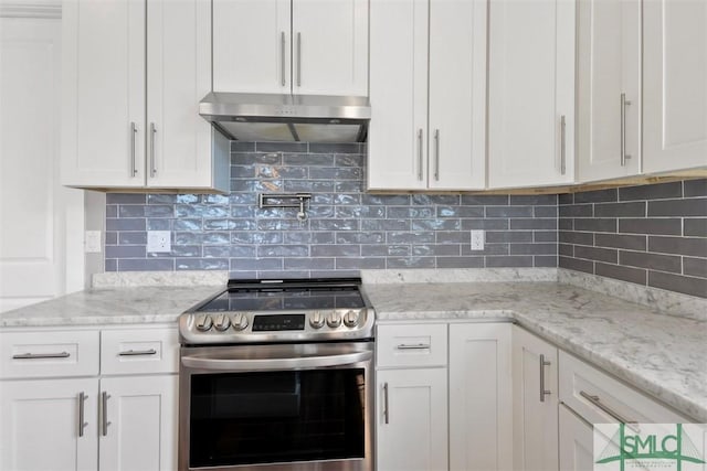 kitchen with light stone counters, under cabinet range hood, stainless steel range with electric cooktop, white cabinets, and tasteful backsplash