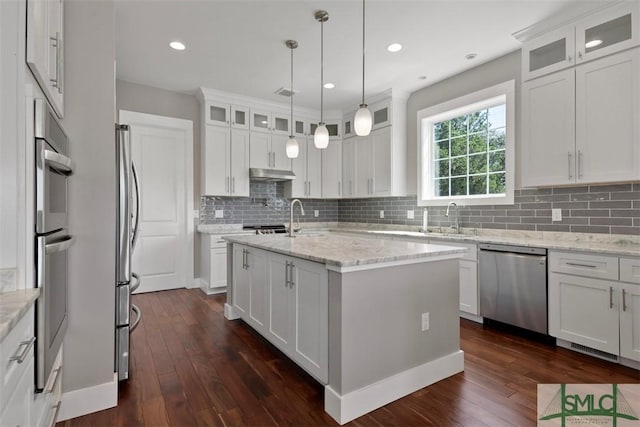 kitchen with dark wood-style flooring, stainless steel appliances, white cabinets, a sink, and under cabinet range hood