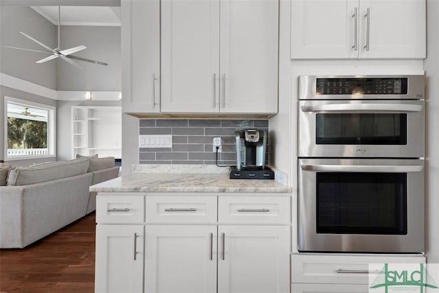 kitchen featuring decorative backsplash, a ceiling fan, open floor plan, crown molding, and stainless steel double oven