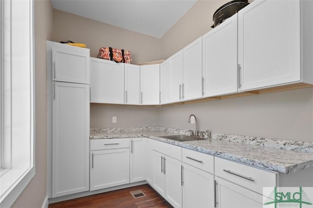 kitchen featuring light stone counters, visible vents, dark wood-type flooring, white cabinets, and a sink