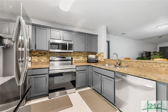 kitchen with sink, tasteful backsplash, gray cabinets, stainless steel appliances, and light stone countertops