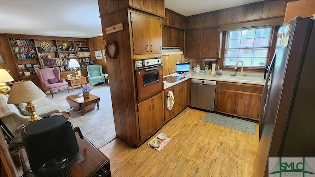 kitchen with sink, wooden walls, stainless steel appliances, and light carpet