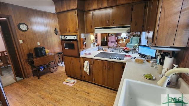 kitchen featuring wooden walls, light wood-type flooring, sink, and oven