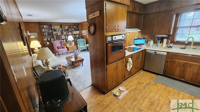 kitchen featuring wooden walls, wall oven, dishwasher, sink, and light colored carpet