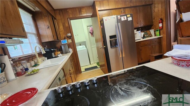 kitchen featuring sink, stainless steel appliances, washer / clothes dryer, and wooden walls