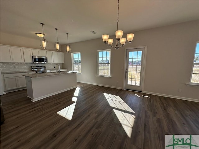 kitchen with a center island with sink, stainless steel appliances, white cabinets, decorative backsplash, and pendant lighting