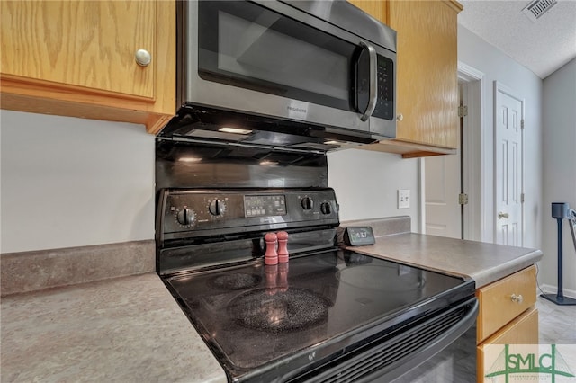 kitchen with black stove, light brown cabinets, and a textured ceiling