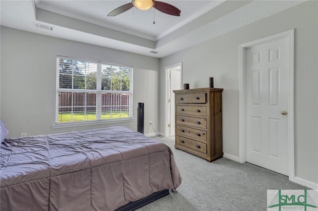 bedroom with ceiling fan, a tray ceiling, and light colored carpet