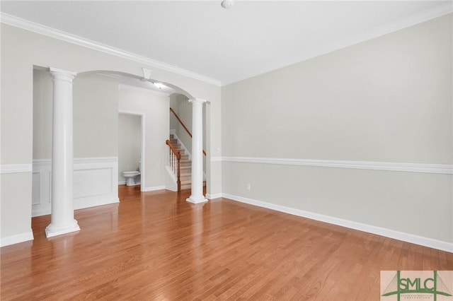 empty room with decorative columns, hardwood / wood-style floors, and crown molding