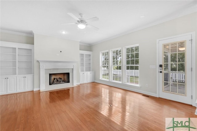 unfurnished living room featuring ceiling fan, crown molding, a fireplace, light wood-type flooring, and built in features