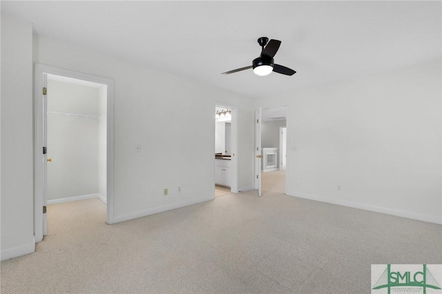 unfurnished bedroom featuring a closet, a spacious closet, connected bathroom, ceiling fan, and light colored carpet