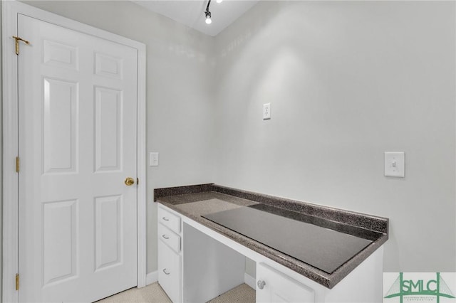 interior space featuring white cabinets, built in desk, and track lighting