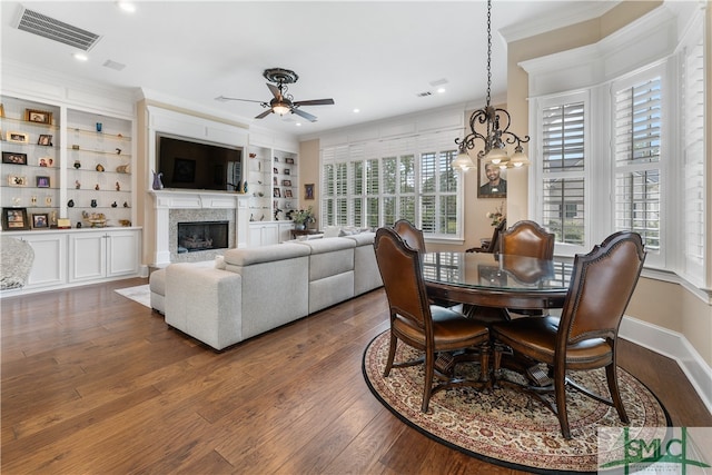 dining area with ceiling fan with notable chandelier, ornamental molding, built in shelves, and dark hardwood / wood-style floors