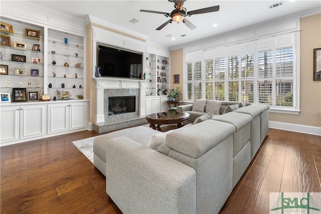 living room featuring ceiling fan, built in shelves, dark hardwood / wood-style floors, ornamental molding, and a premium fireplace