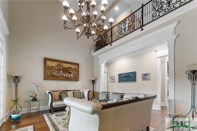 living room with a notable chandelier, decorative columns, hardwood / wood-style flooring, and a towering ceiling