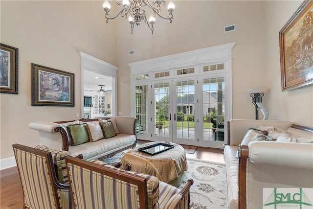 living room with a towering ceiling, french doors, ceiling fan with notable chandelier, and wood-type flooring