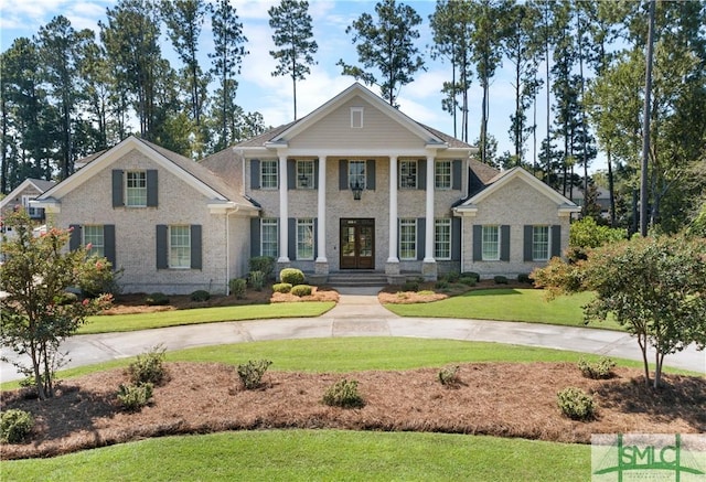 greek revival inspired property featuring french doors, driveway, and a front lawn