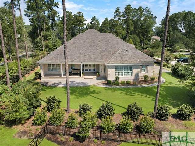 view of front of house with a patio area, a shingled roof, a front lawn, and fence