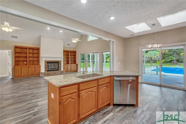 kitchen with vaulted ceiling with skylight, a fireplace, sink, stainless steel dishwasher, and a center island with sink