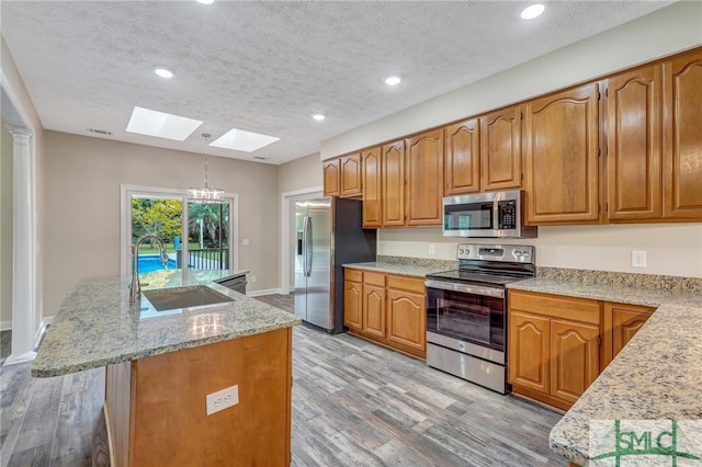 kitchen with a skylight, stainless steel appliances, hanging light fixtures, and hardwood / wood-style flooring