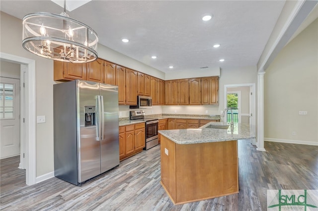 kitchen featuring appliances with stainless steel finishes, light hardwood / wood-style floors, light stone countertops, decorative light fixtures, and sink