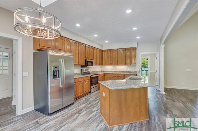 kitchen with pendant lighting, sink, stainless steel appliances, light stone counters, and a kitchen island