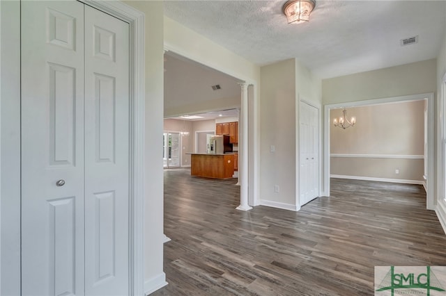 unfurnished living room with a textured ceiling, decorative columns, dark hardwood / wood-style flooring, and a chandelier