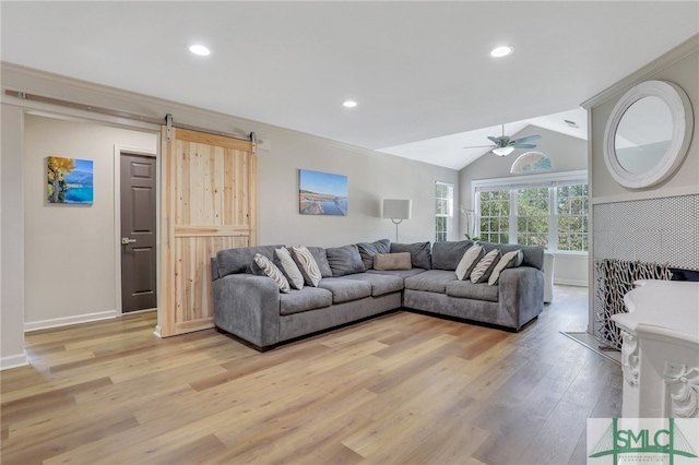 living room with lofted ceiling, a barn door, light wood-type flooring, and ceiling fan