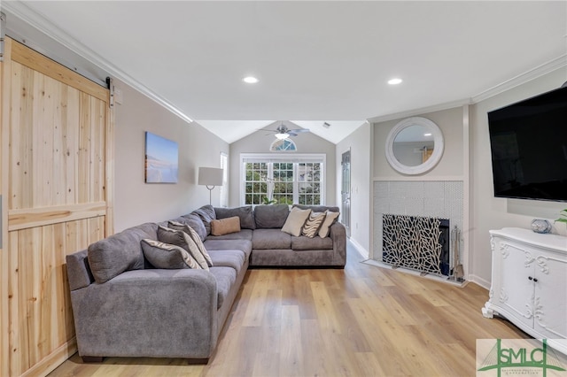 living room with a tile fireplace, lofted ceiling, light hardwood / wood-style floors, ceiling fan, and a barn door