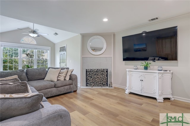 living room with a tiled fireplace, light hardwood / wood-style flooring, vaulted ceiling, and ceiling fan