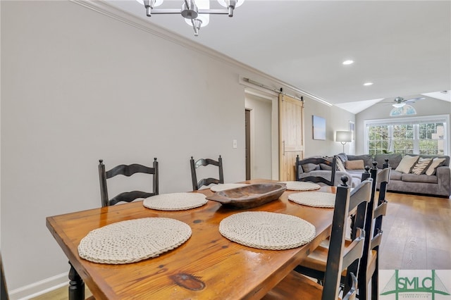 dining area featuring ceiling fan with notable chandelier, ornamental molding, hardwood / wood-style flooring, vaulted ceiling, and a barn door