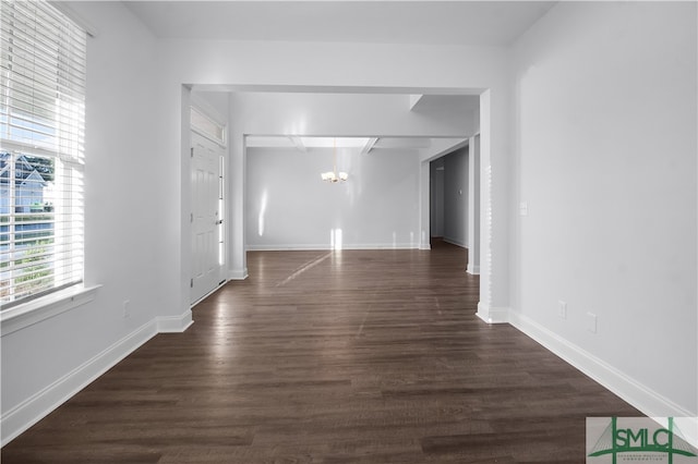 spare room featuring an inviting chandelier and dark wood-type flooring