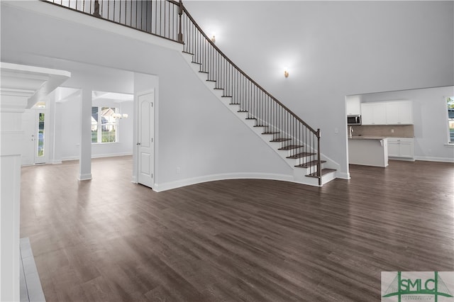 unfurnished living room featuring a towering ceiling, a chandelier, and dark wood-type flooring