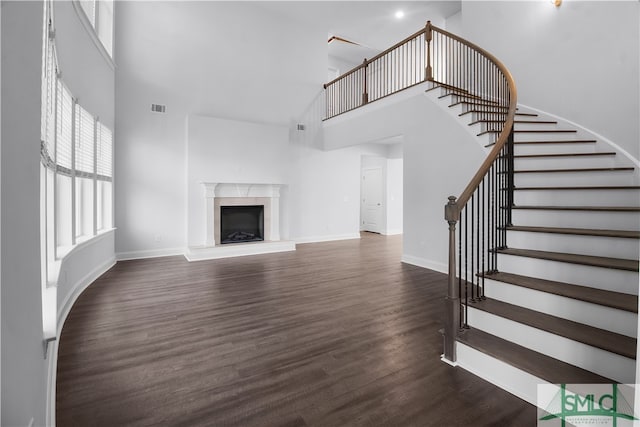 unfurnished living room with a high ceiling, dark wood-type flooring, and a fireplace