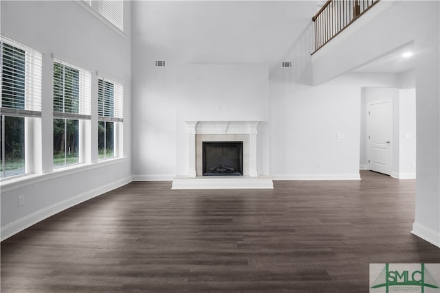 unfurnished living room with a tile fireplace, a towering ceiling, and dark hardwood / wood-style flooring